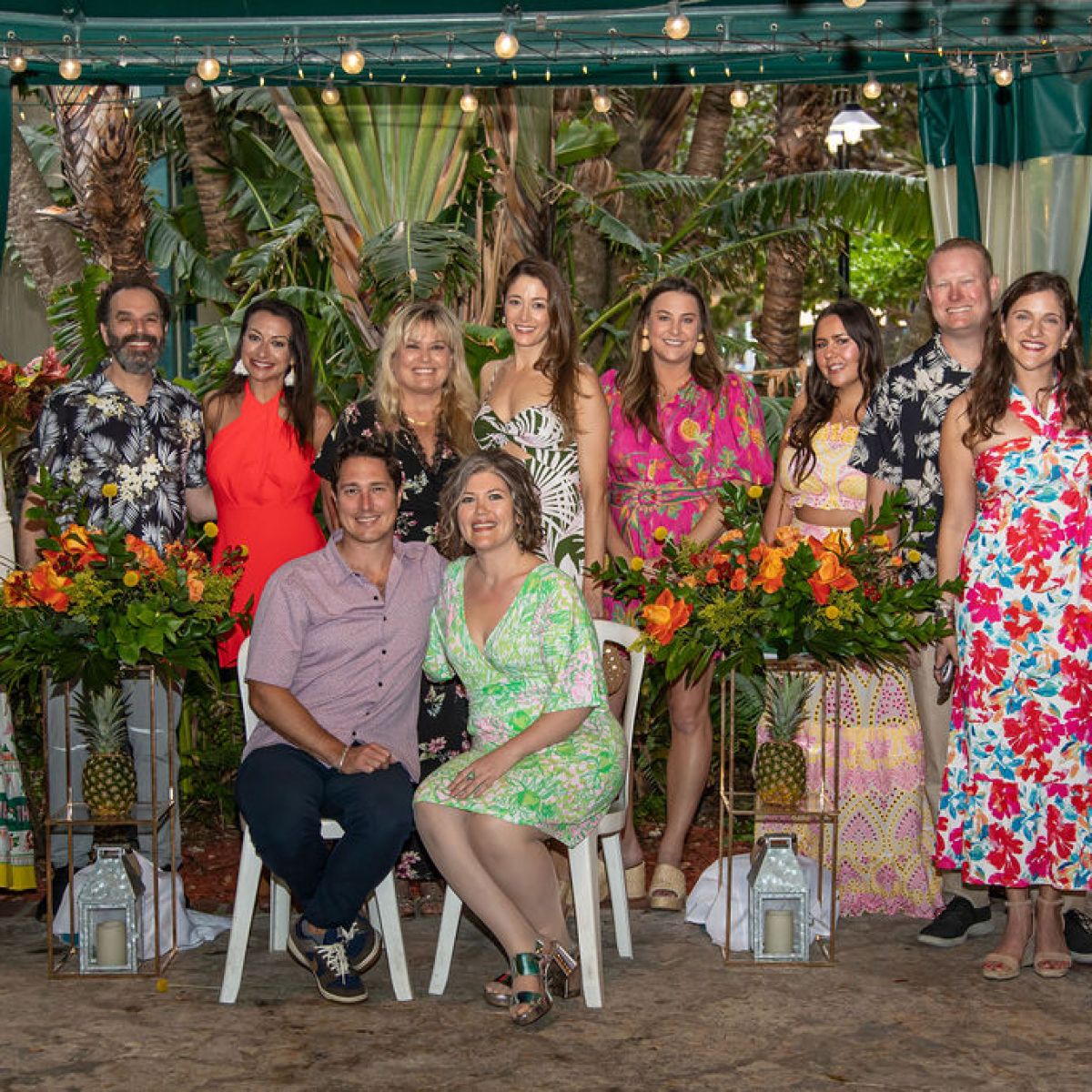 Group of people posing in colorful attire indoors with floral arrangements.