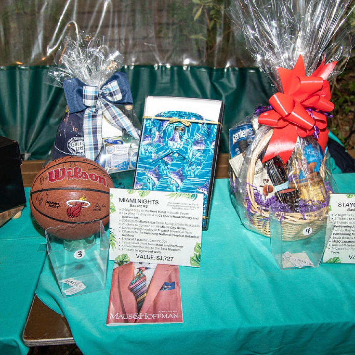 Gift baskets with items including a basketball, displayed on a turquoise table with description cards.