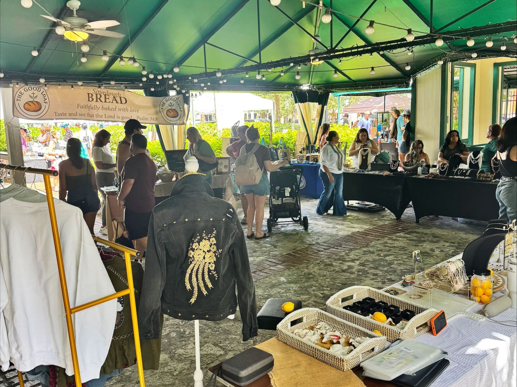 Indoor market scene with people browsing stalls under a green canopy with hanging lights.