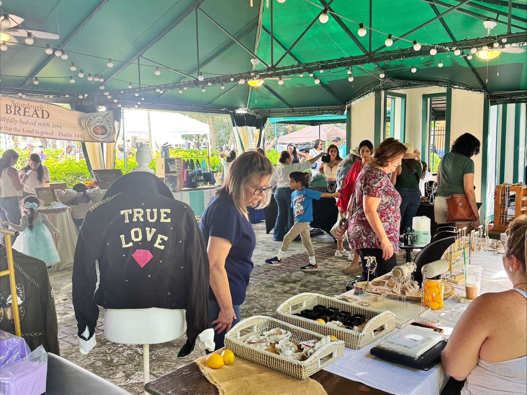 Market scene with people and stalls under a green canopy, jacket with 'True Love' displayed.
