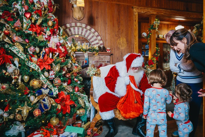 Santa with children near a decorated Christmas tree in a cozy wooden room.